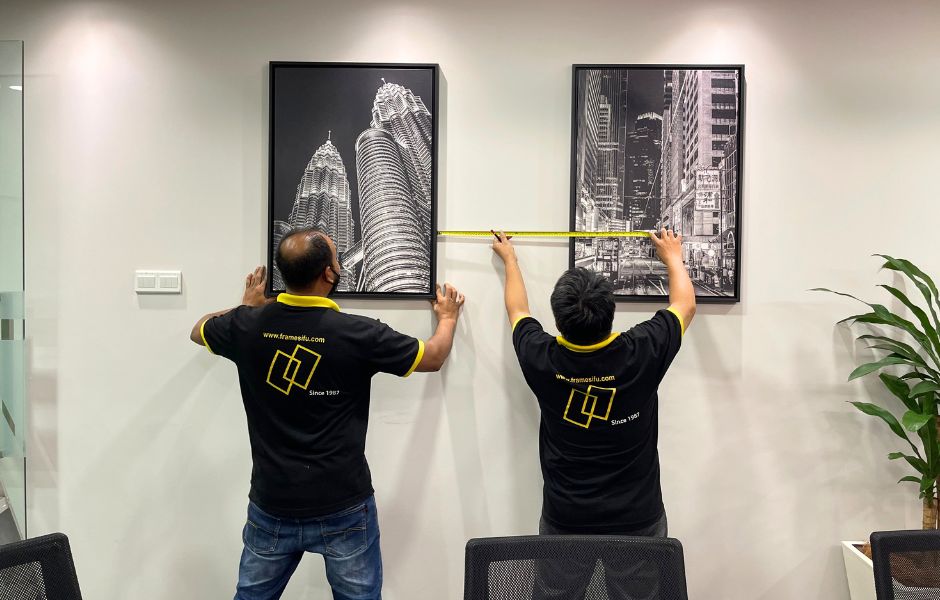 Frame Sifu team measuring and installing framed city-skyline prints on a living room wall in Malaysia